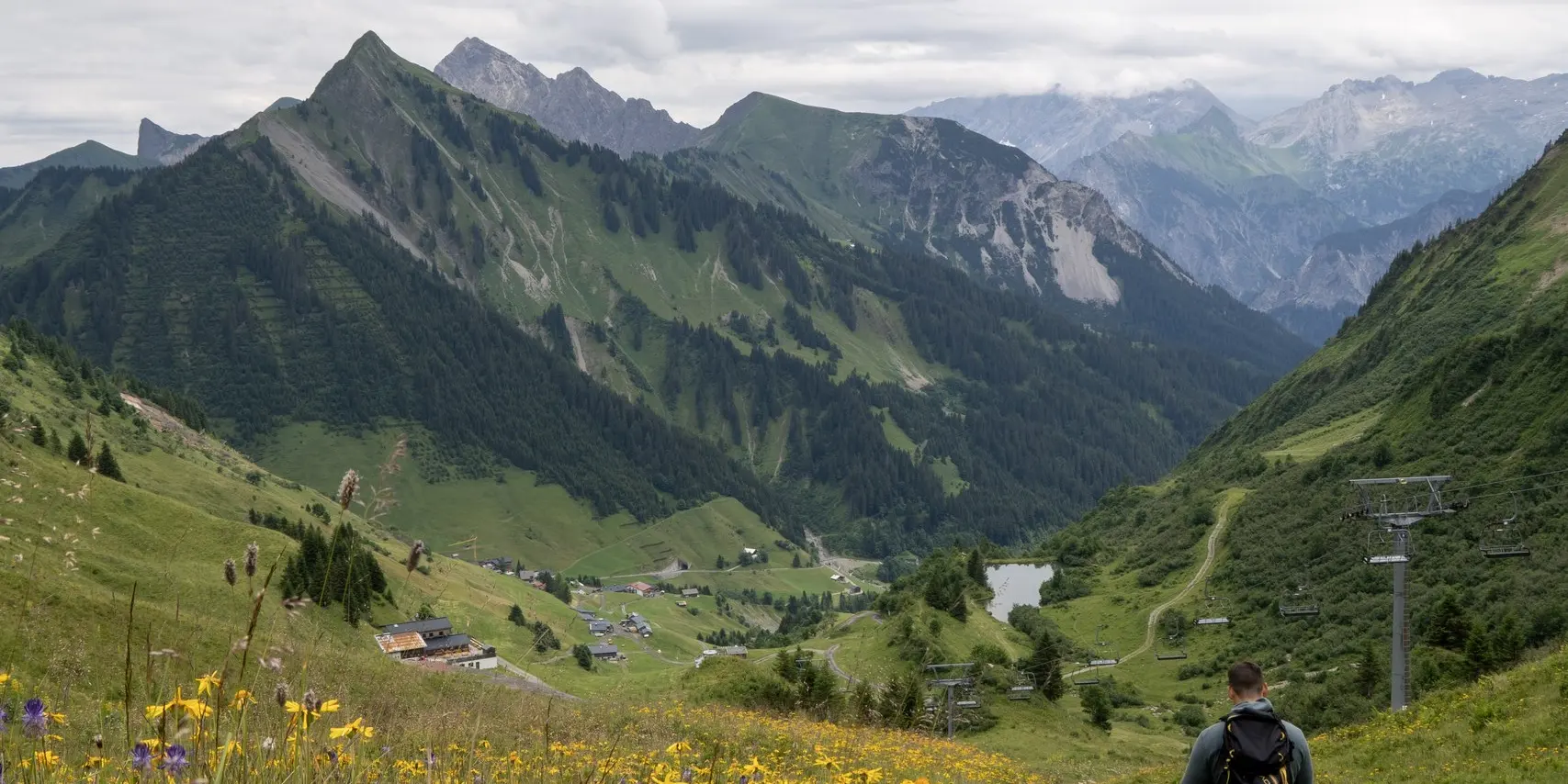 Wanderer auf einer Blumenwiese vor Bergkulisse