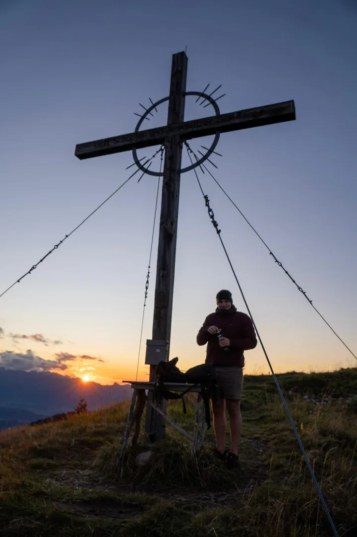 Wanderer am Gipfelkreuz bei Sonnenuntergang