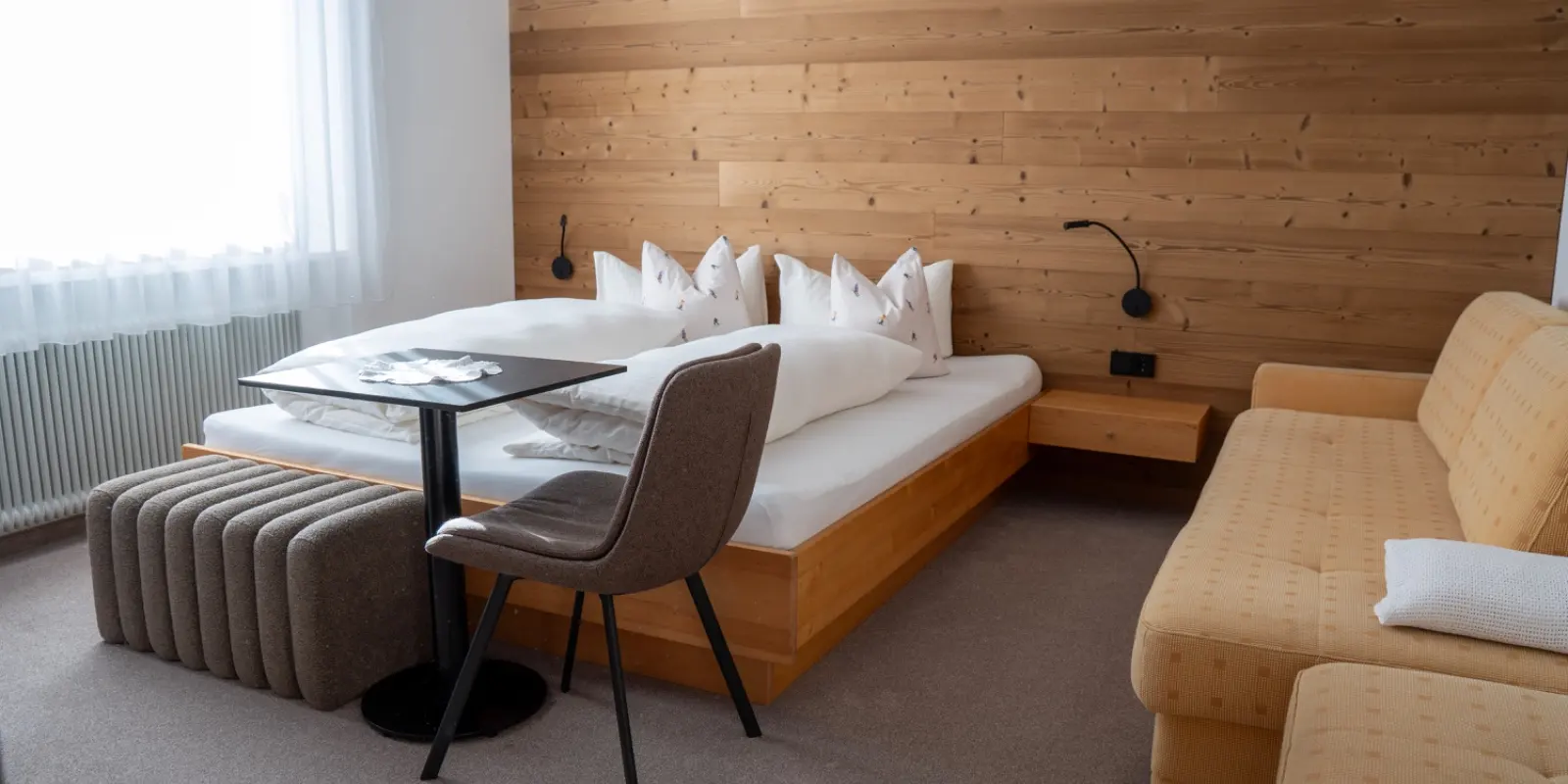Schlafzimmer mit Doppelbett, kleinem Tisch und Couch vor der Holzwand