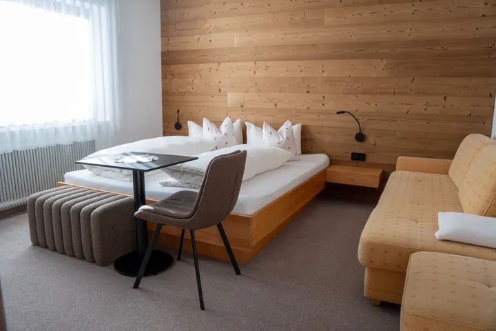 Schlafzimmer mit Doppelbett, kleinem Tisch und Couch vor der Holzwand